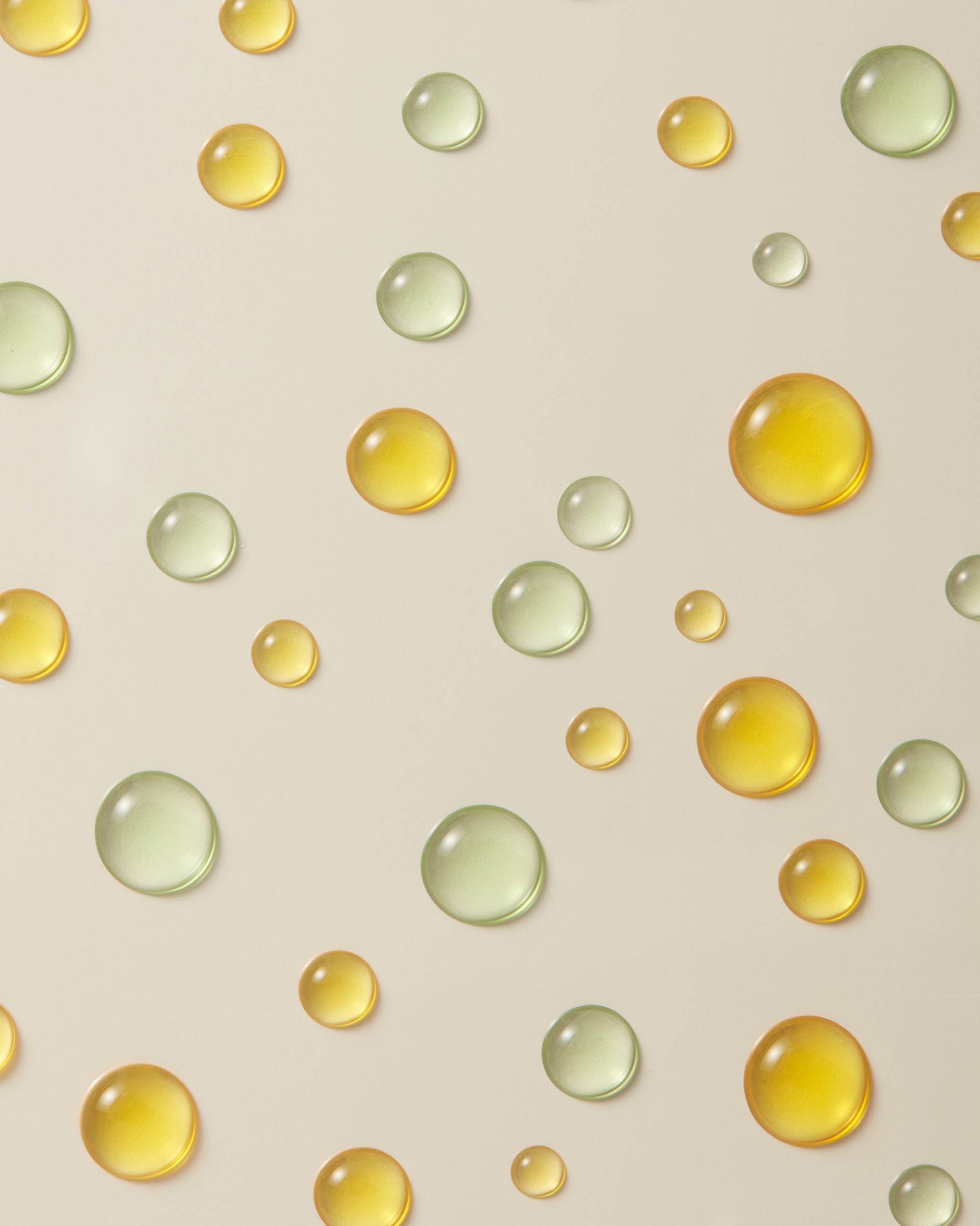 golden orange and green skincare oil droplets on a light grey tan surface
