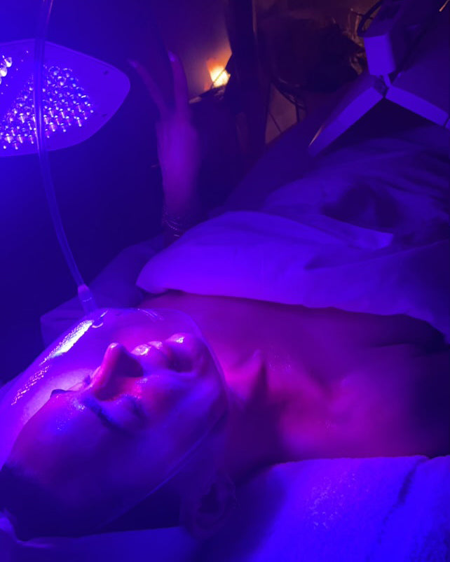 Victoria Lampley Berens under blue LED lamp during facial with Jackie Park