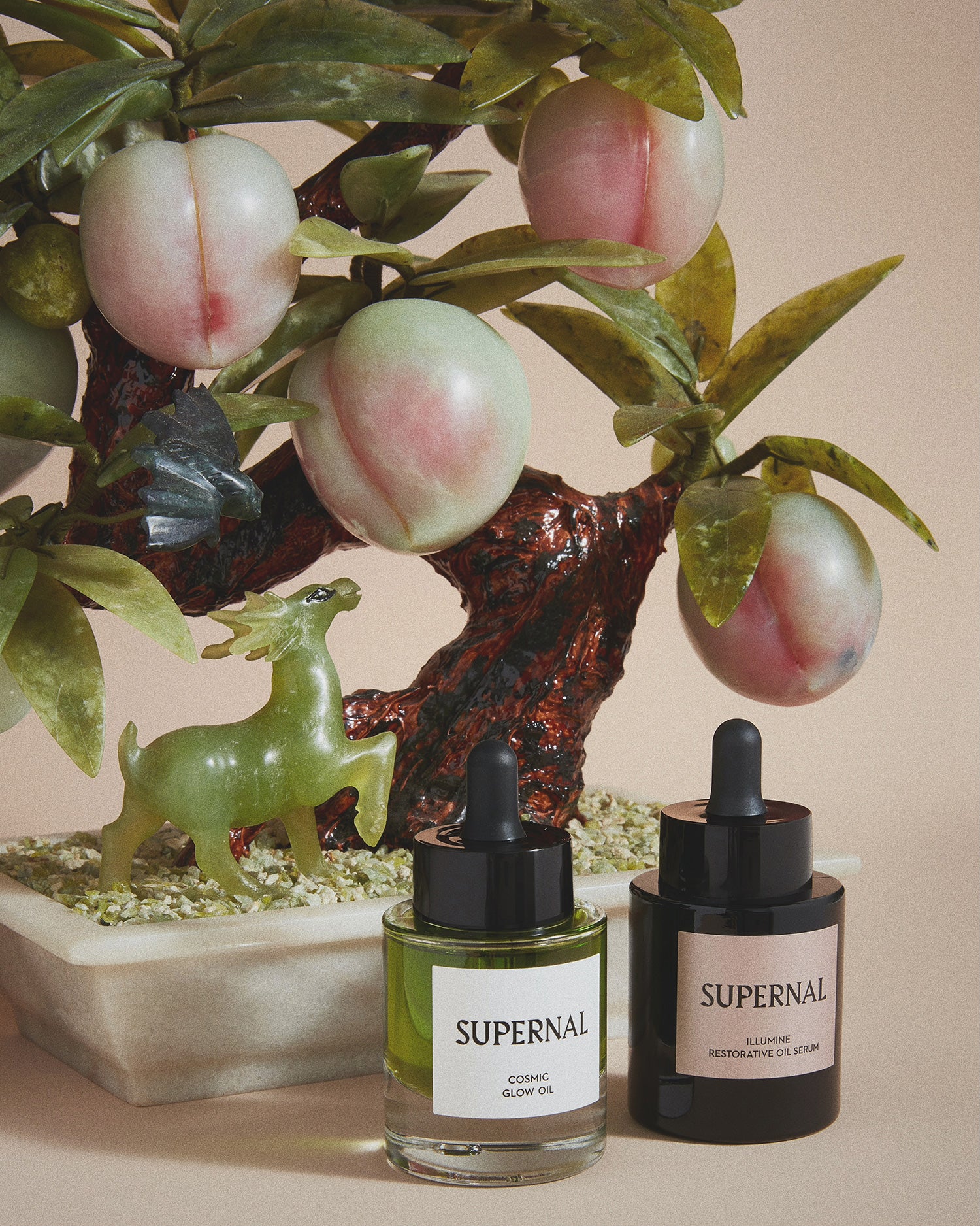 Clear Glass green face oil and black glass skincare bottle next to Jade plum tree statue on taupe colored background