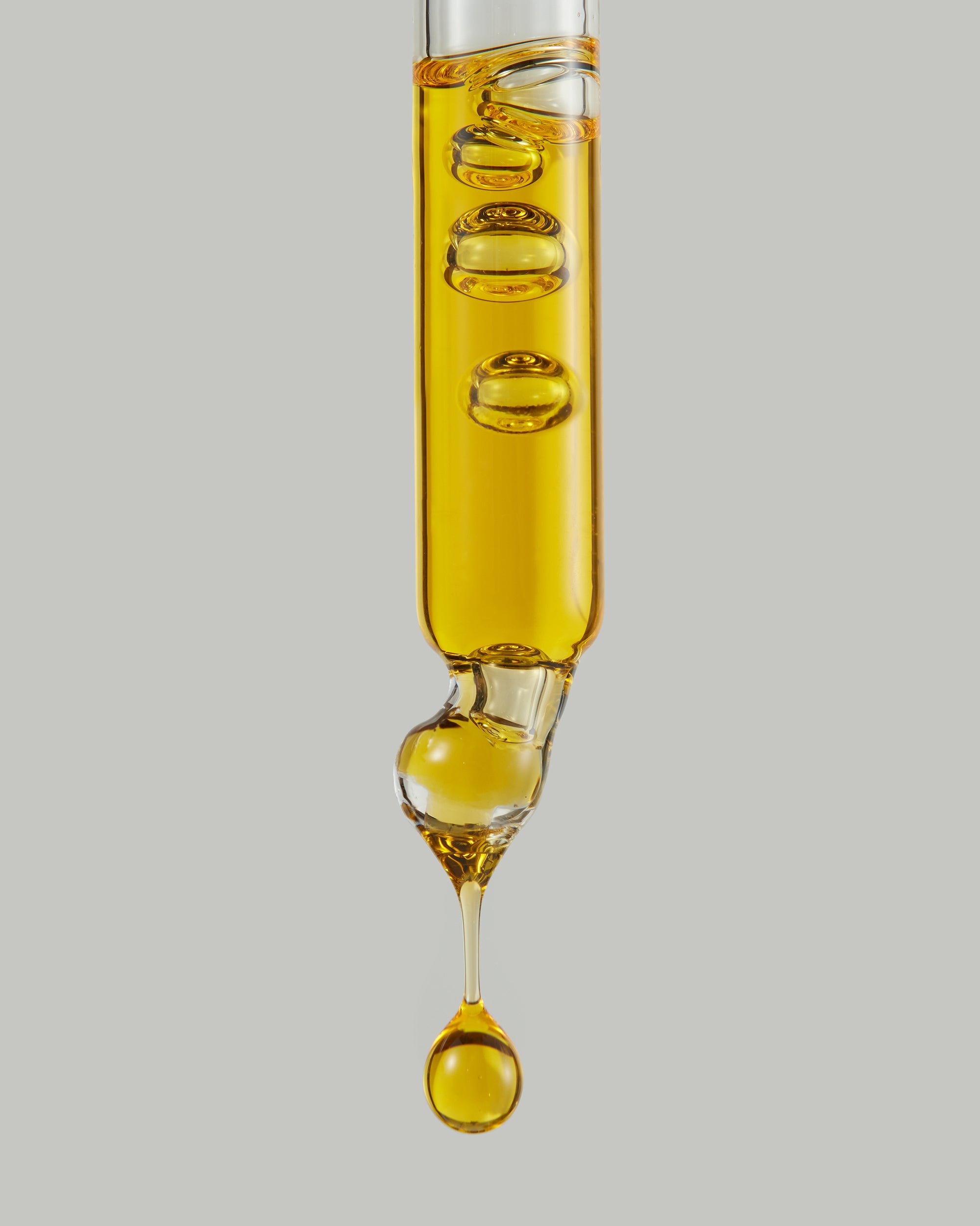 golden orange skincare oil dripping from a glass pipette on grey background